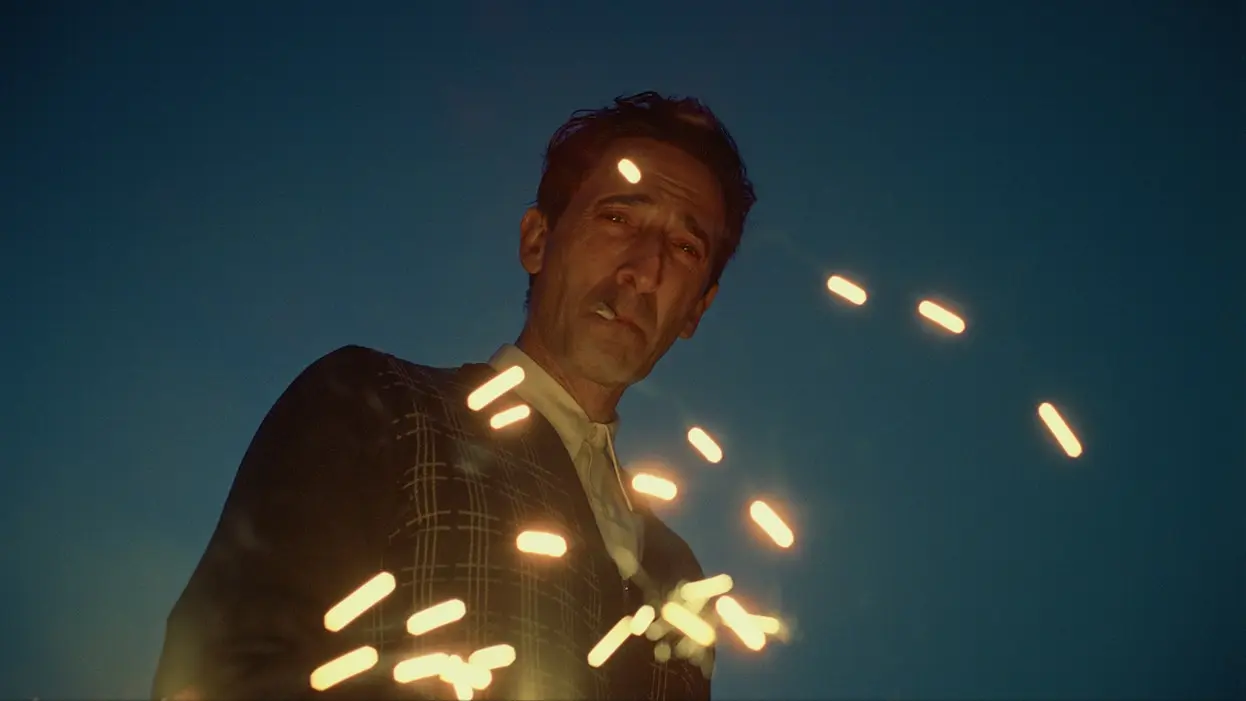 The character, László Tóth (played by Adrien Brody), looks at the camera smoking a cigarette.