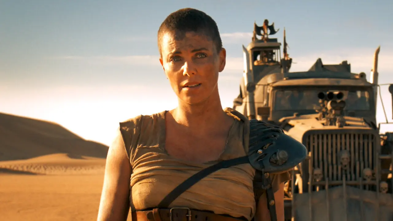 Furiosa (Charlize Theron) stands in the desert in front of a truck.