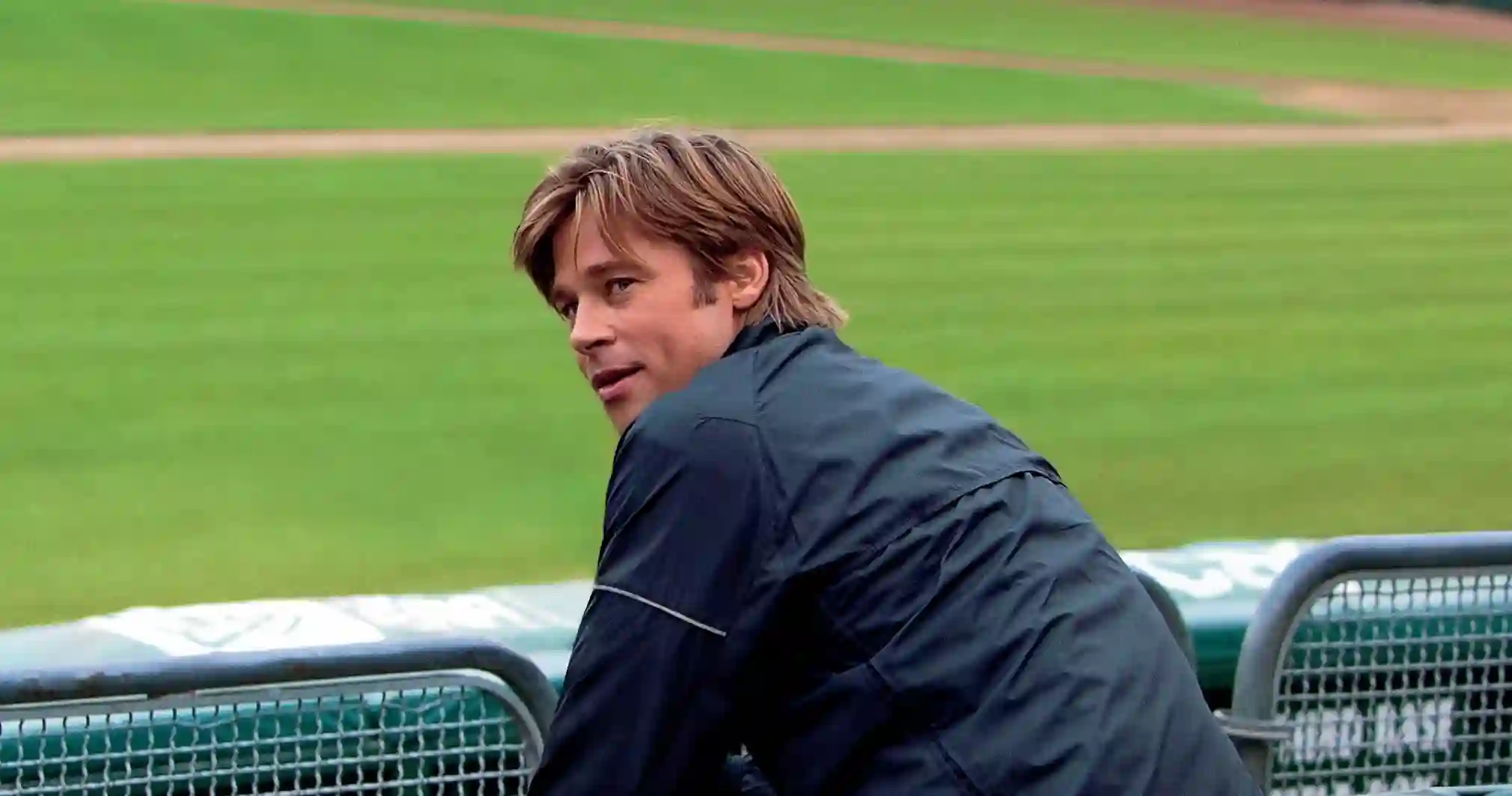 Brad Pitt sits in a baseball stadium.